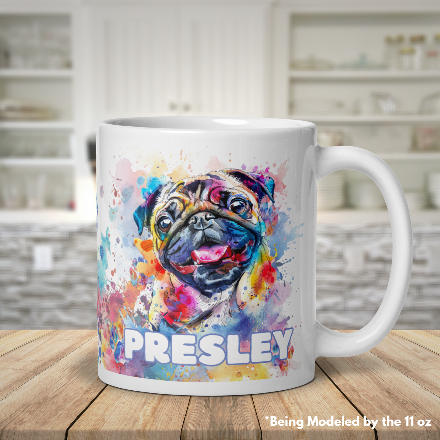 11 oz mug with the custom name of Presley on it. There are splashes of watercolor, a very cute and happy pug smiling with its tongue out and little watercolor soaked paw prints all over the mug. The base of the mug is white. The coffee, tea, soup cup is sitting on a wooden surface with a blurred white kitchen behind it.