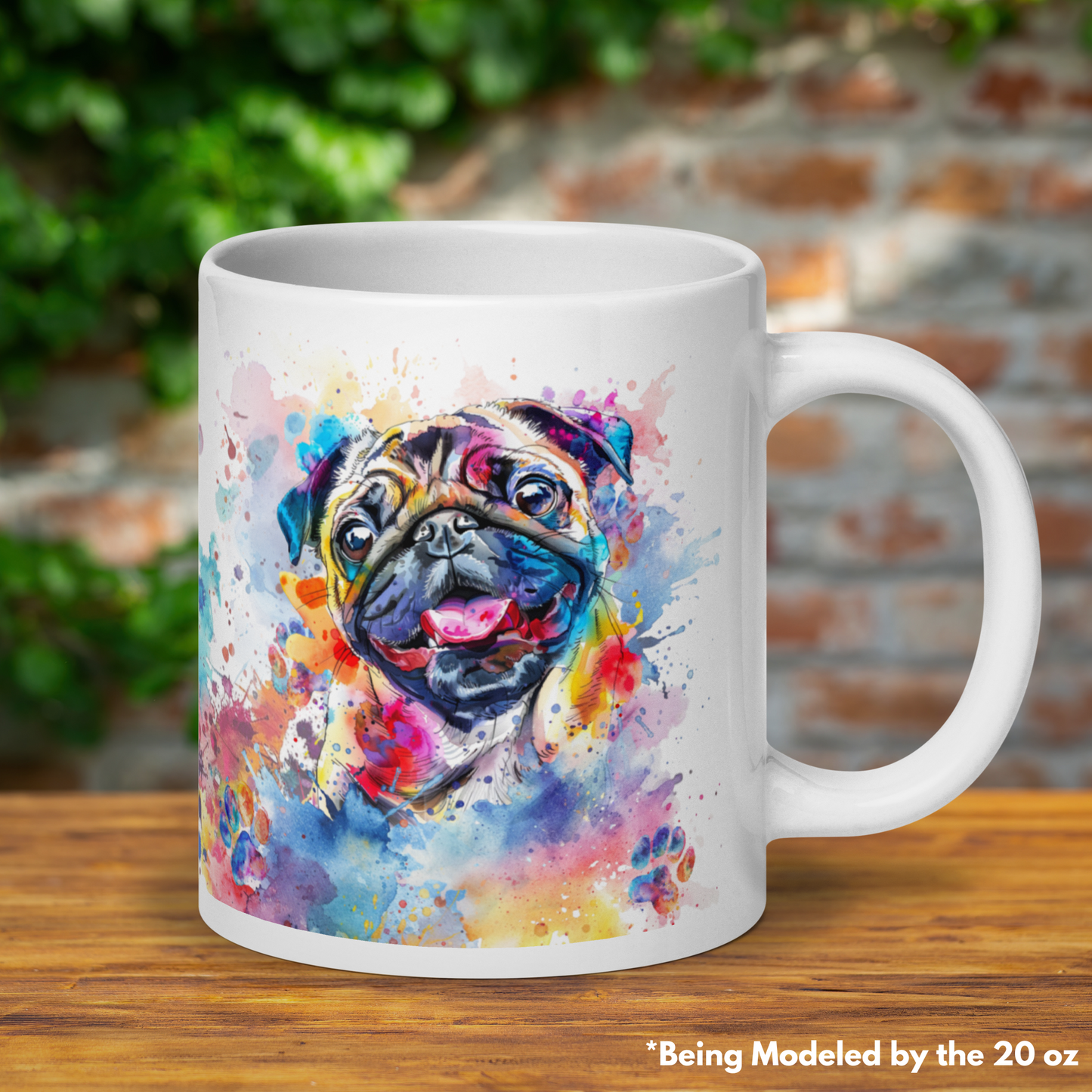 20 oz mug with the option of not having a name on it. There are splashes of watercolor, a very cute and happy pug smiling with its tongue out and little watercolor soaked paw prints all over the mug. The base of the mug is white. The coffee, tea, soup cup is sitting on a wooden surface with a blurred brick wall and vine behind it.