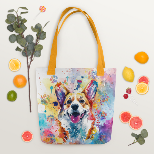 Corgi Craze Watercolor Tote Bag. The tote bad has a Corgi dog in watercolor drawing with watercolor splashes and paw prints, yellow handle, laying down on surface fruit and candy around the bag.