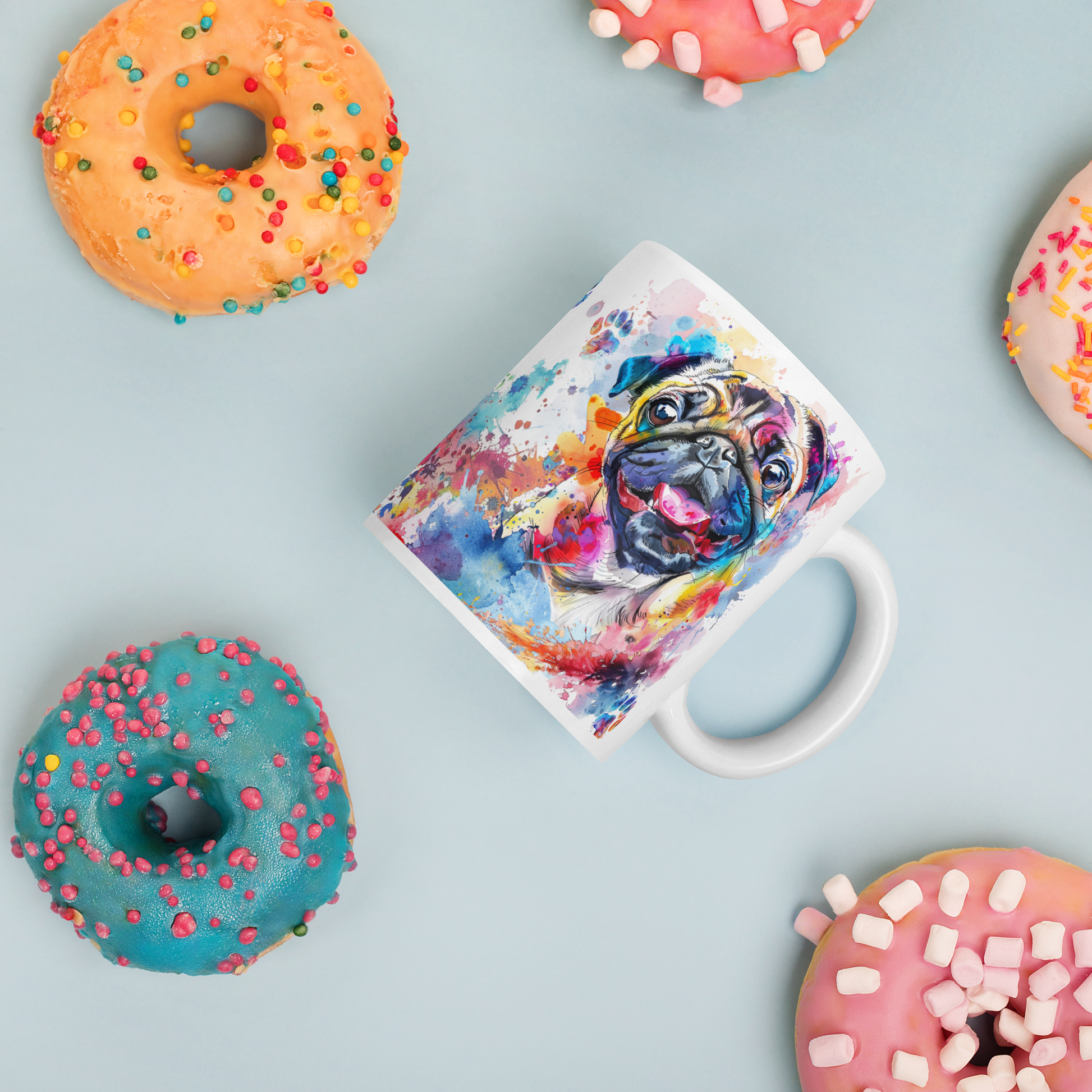 Doggone Proud Pug Dog Mug. A fun colorful mug with handle showing a happy Pug dog surrounded by watercolor splashes, clouds, and paws. Mug is laying flat with donuts around it.