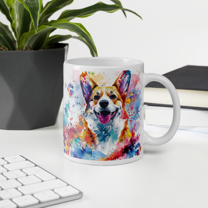 Doggone Proud Corgi 11 oz Mug. A fun mug with a happy Corgi dog surrounded by watercolor splashes, clouds, and paws. Mug is on a white desk with a plant book and keyboard. Great give for any dog lover or paw-rent.