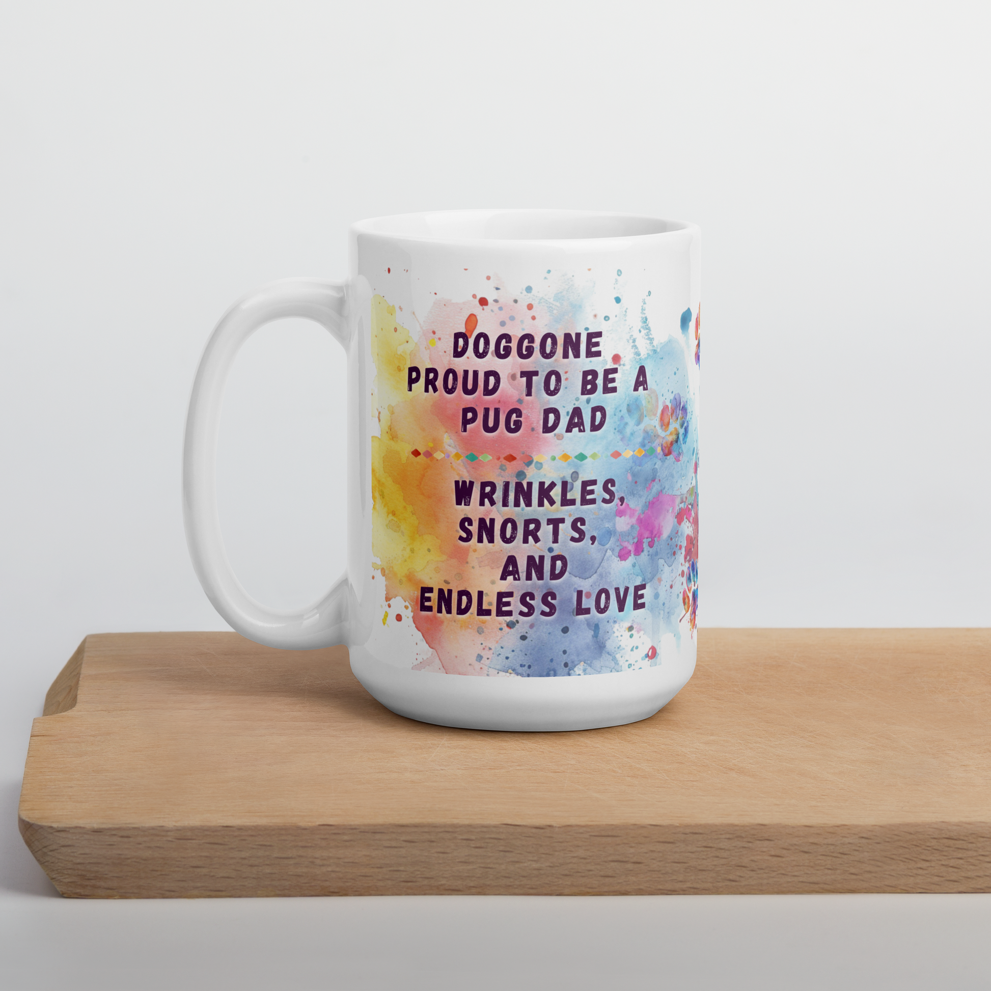 Doggone Proud Pug Dog Dad Mug. Mug with handle on left showing a cute quote: Doggone Proud to be a Pug Dad, Wrinkles, Snorts, and Endless Love. The quote is surrounded by colorful and fun watercolor splashes & paws. On a wood board.