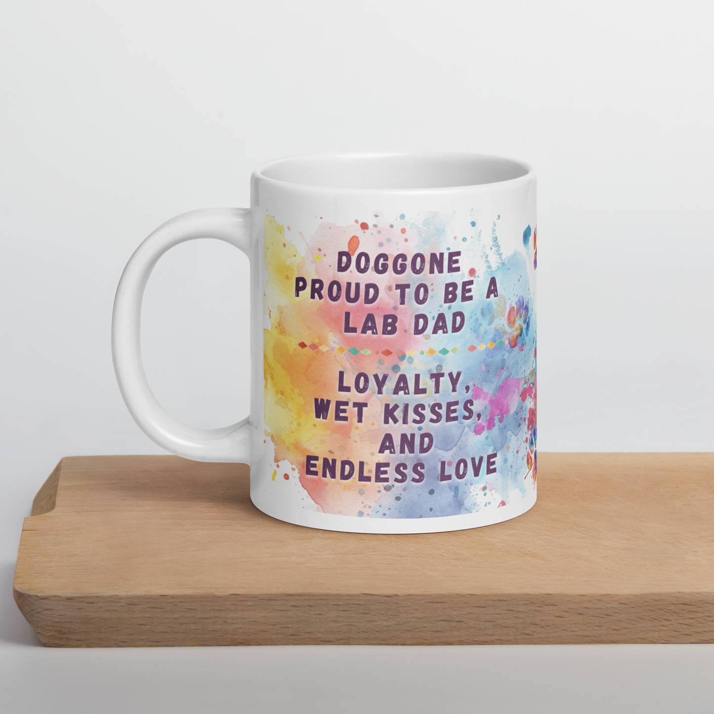 Doggone Proud Lab Dog Dad Mug. Mug with handle on left showing a cute quote: Doggone Proud to be a Lab Dad, Loyalty, Wet Kisses, and Endless Love. The quote is surrounded by colorful and fun watercolor splashes & paws. On a wood board.